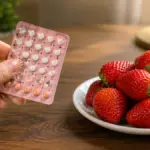 hand holding birth control blister pack next to fresh strawberries
