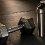 iron dumbbell resting next to a silver shaker bottle on a gym mat gym