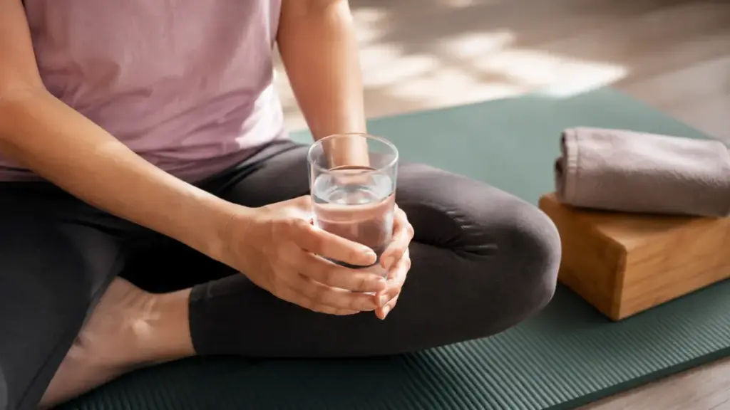 person-resting-on-a-yoga-mat-holding-a-glass-of-water