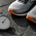 silver sports stopwatch resting next to running shoes on stone