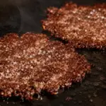 sizzling hot thin smash burger patties with crisp caramelized edges on a cast iron griddle