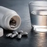 spill of metallic pills from a white jar on a slate table