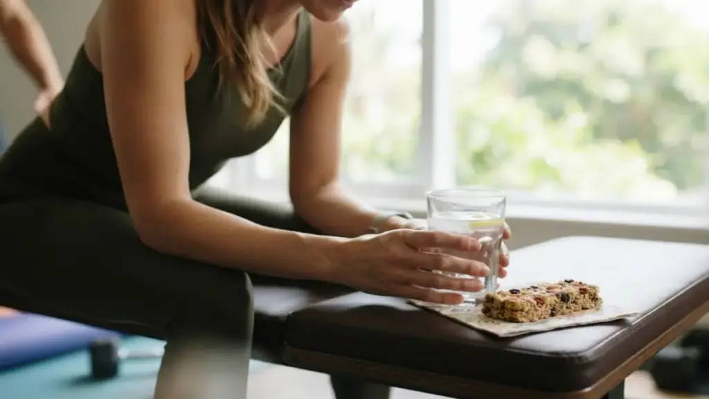 woman-resting-on-a-bench-holding-a-glass-of-water-near-a-protein-bar